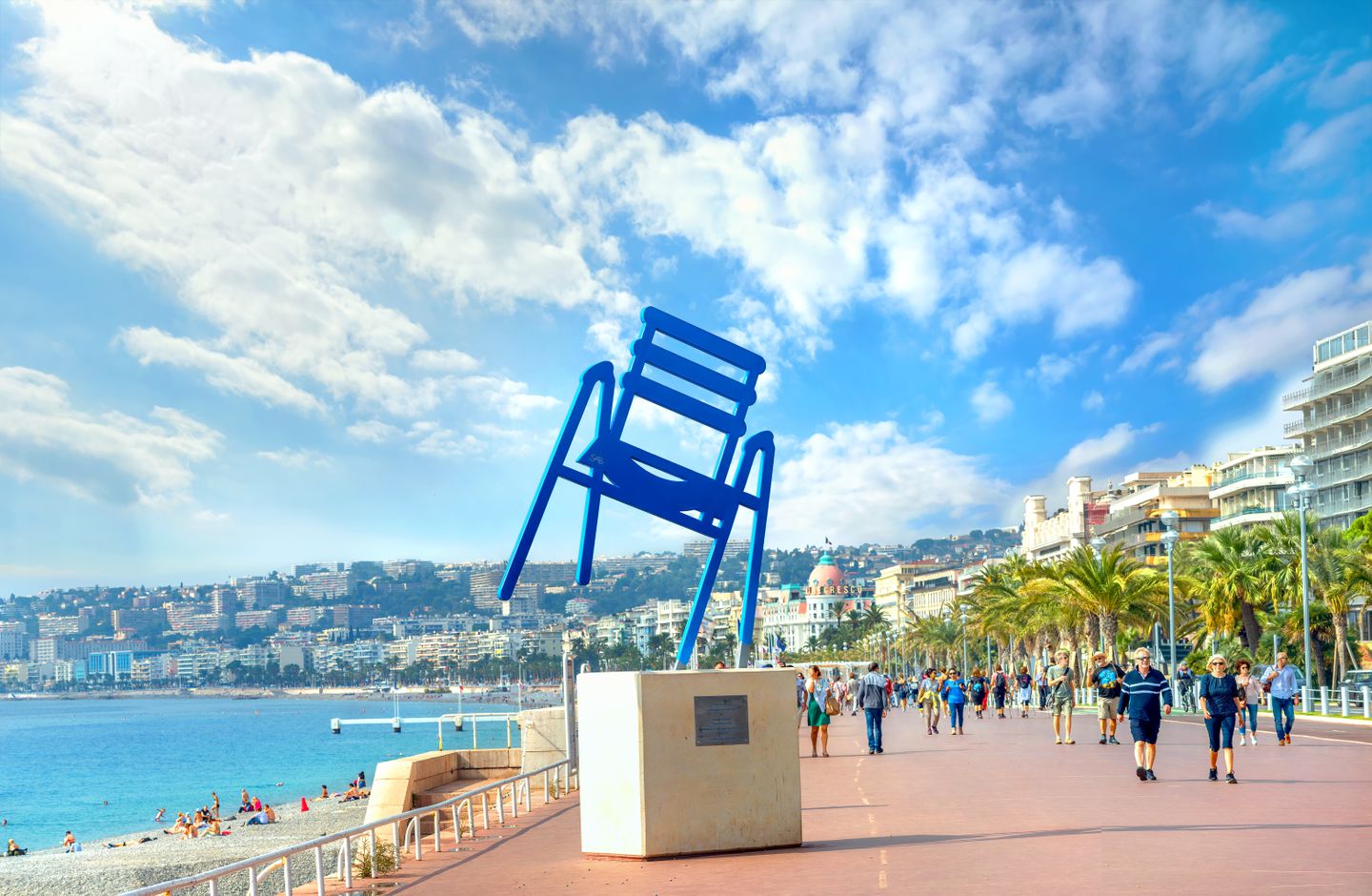  People walking along the Promenade des Anglais past a sculpture of the famous blue chair (artist Sabine Geraudie)