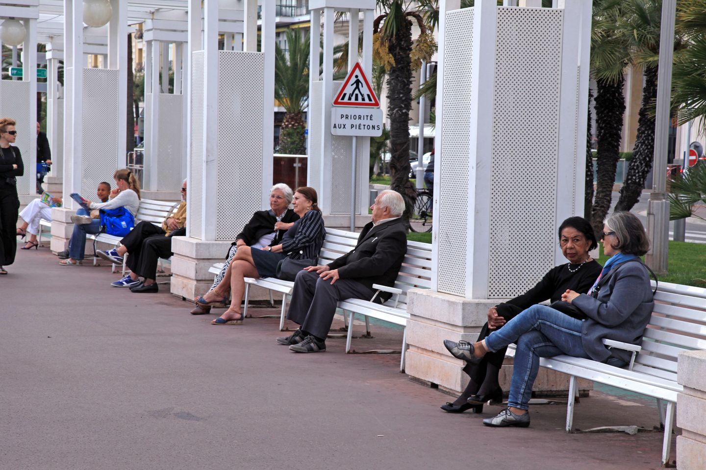 People sitting and chatting on benches on the Promenade des Anglais in Nice, France