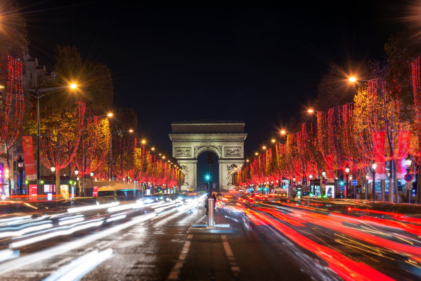 Champs Elysees avenue and the Arc de Triomphe decorated with red Christmas lights at night in Paris, France.
